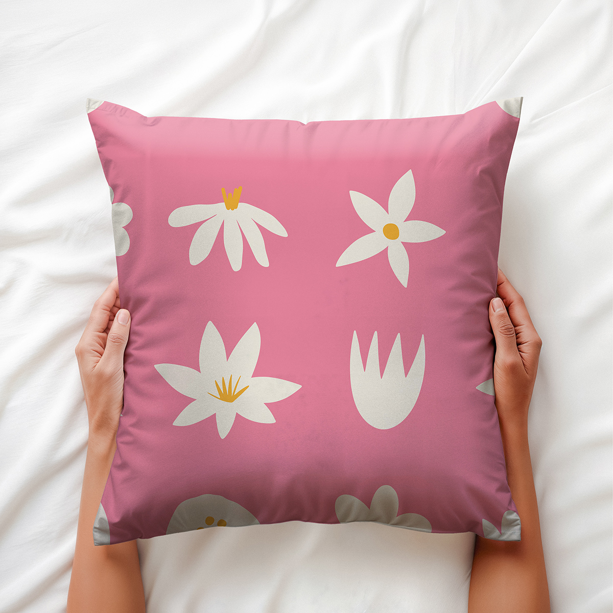 Ręce trzymające różową poduszkę w kwiatowy wzór na białej pościeli