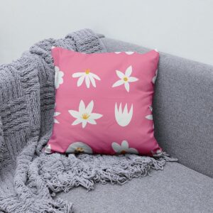 Poduszka z motywem stokrotek ułożona na szarej sofie obok plecionego koca