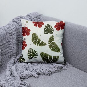 Poduszka z motywem tropikalnym ułożona na sofie obok szarego koca, aranżacja wnętrza