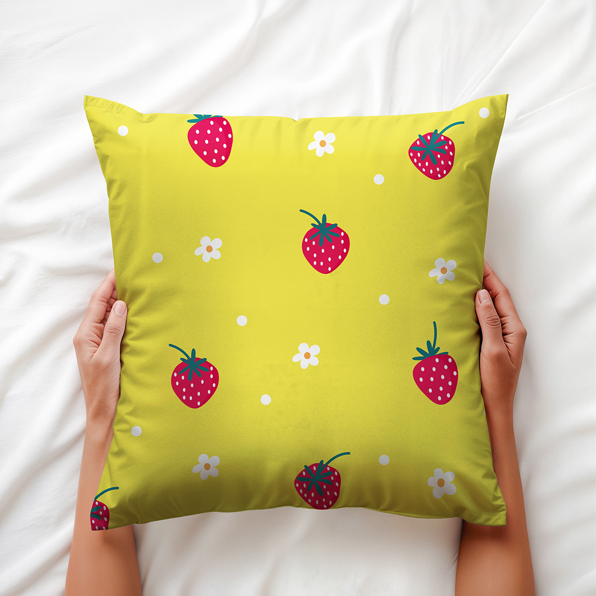 Ręce trzymające poduszkę z truskawkowym wzorem na białej pościeli — ujęcie aranżacyjne