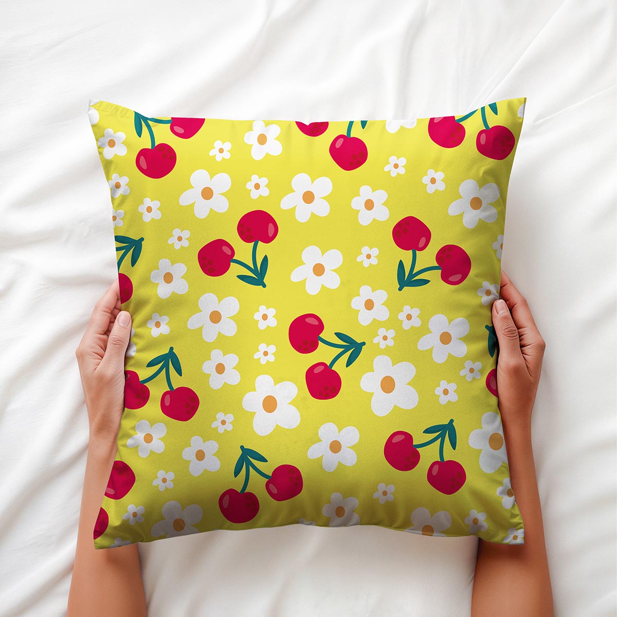 Aranżacyjne ujęcie: osoba trzyma poduszkę z wiśniami i stokrotkami na białej pościeli