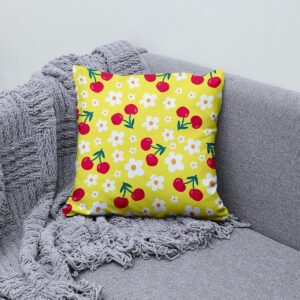Detal aranżacyjny: poduszka z wiśniami i stokrotkami na szarej kanapie obok pledu