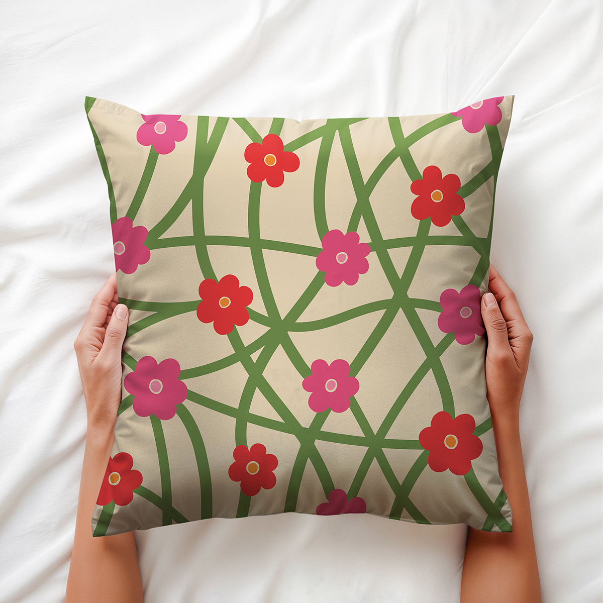 Poduszka trzymana w dłoniach na białej pościeli z widocznym wzorem zielonych pędów i kwiatków