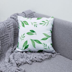 poduszka z akwarelowymi gałązkami ustawiona na szarej sofie z plecionym kocem