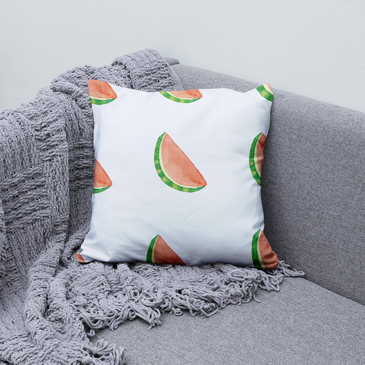 Aranżacja poduszki na sofie z szarym kocem, widoczne powtarzające się plasterki arbuza