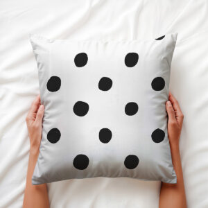 Dłoń trzyma miękką poduszkę z czarnymi kropkami na jasnym tle — ujęcie aranżacyjne