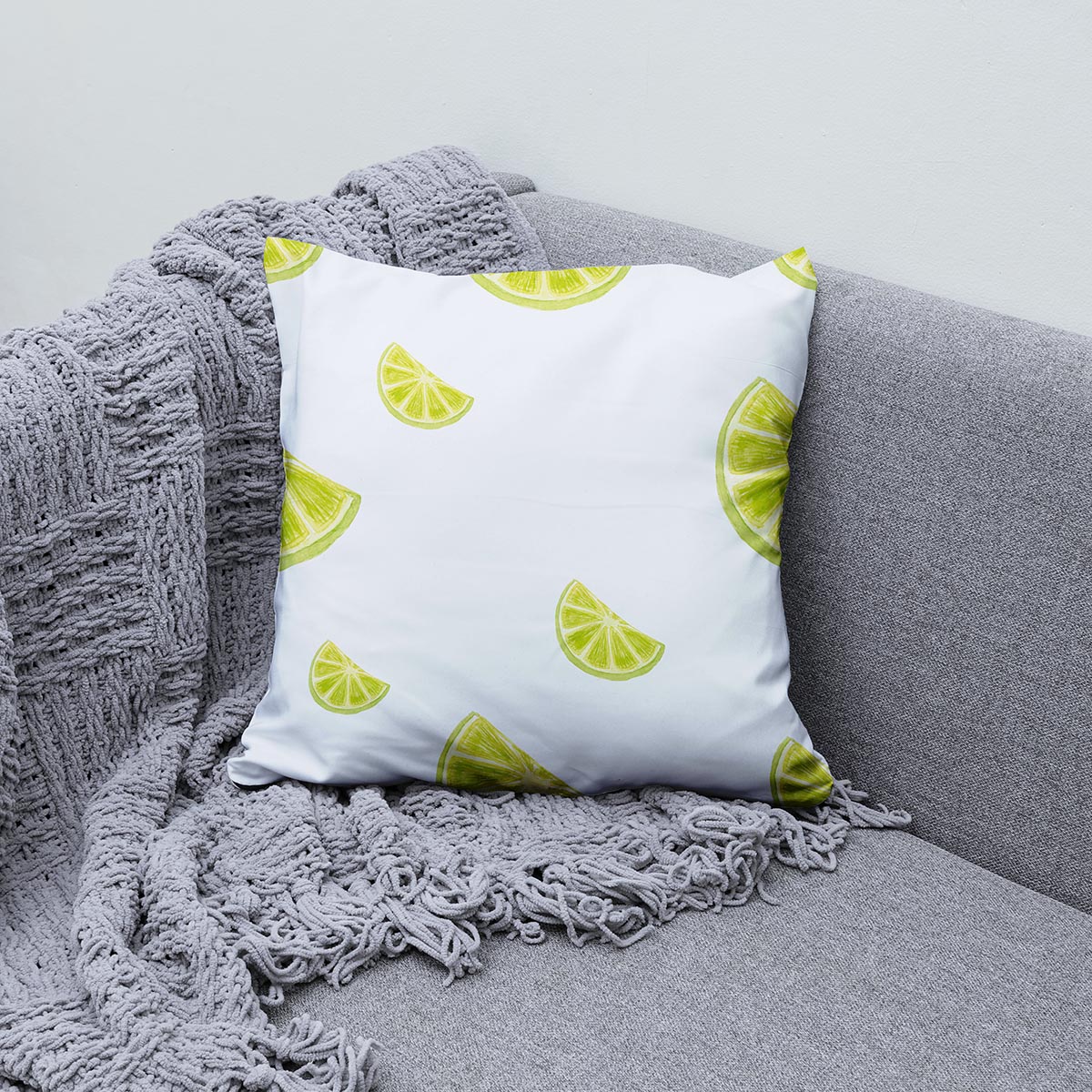 aranżacja poduszki z limonkowymi plasterkami na szarej sofie z pledem
