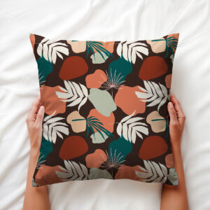 Dłoń trzyma poduszkę ozdobną z roślinnym motywem i ciepłymi, ziemistymi kolorami