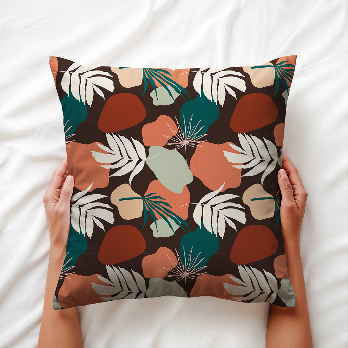 Dłoń trzyma poduszkę ozdobną z roślinnym motywem i ciepłymi, ziemistymi kolorami