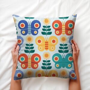 Ręce trzymają poduszkę z geometrycznymi motylami na jasnej pościeli