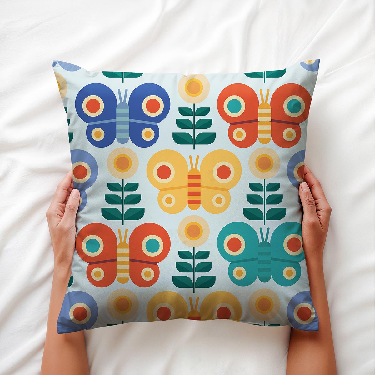 Ręce trzymają poduszkę z geometrycznymi motylami na jasnej pościeli