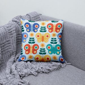 Poduszka z motywem motyli ułożona na szarej sofie obok pledu