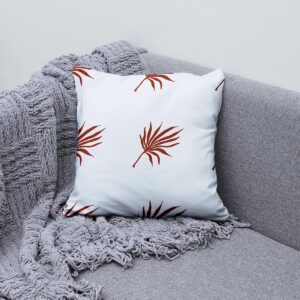 poduszka ozdobna ułożona na kanapie obok pledu, pokazująca wzór palmowych liści w aranżacji