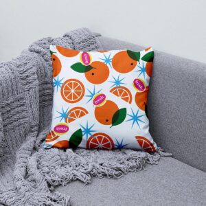 Poduszka dekoracyjna z pomarańczowym wzorem ułożona na kanapie z szarym kocem