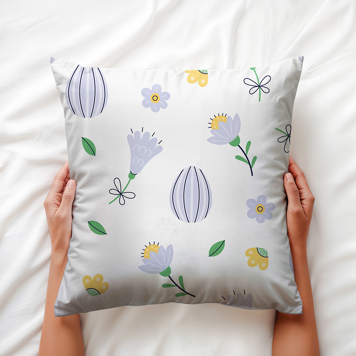 Poduszka trzymana dłońmi na jasnej pościeli, widoczny liliowy motyw kwiatowy