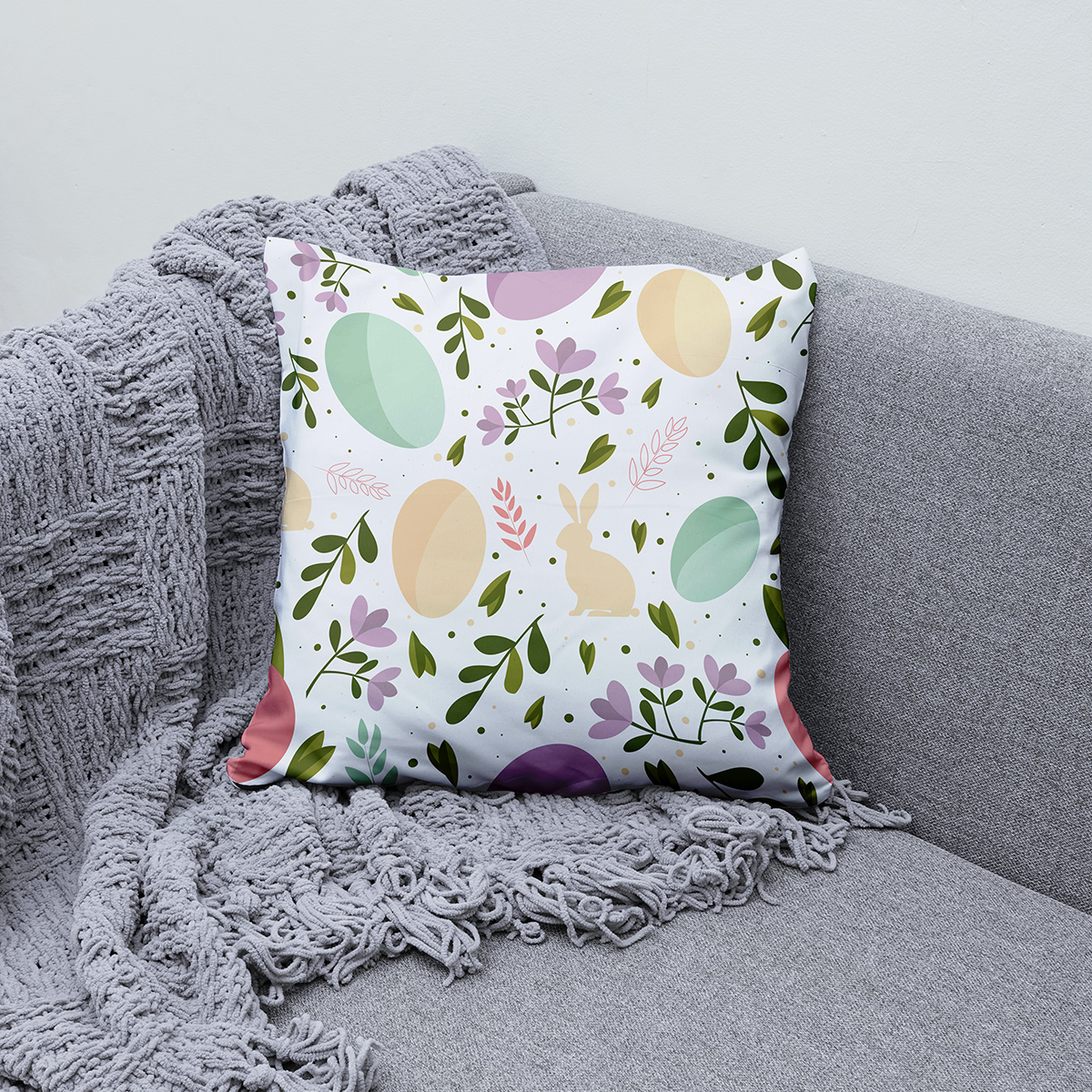 Poduszka z pastelowymi jajkami i kwiatami ułożona na kanapie