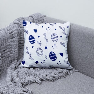 Poduszka z motywem pisanek ułożona na kanapie obok plecionego koca
