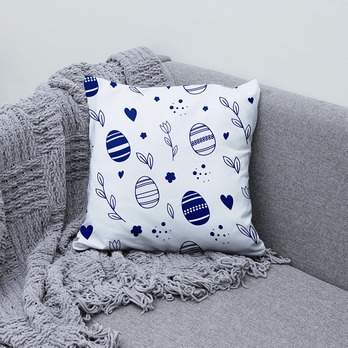 Poduszka z motywem pisanek ułożona na kanapie obok plecionego koca