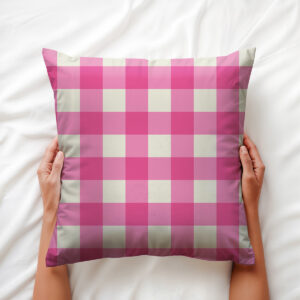 Dłonie trzymające poduszkę dekoracyjną w różowo-kremową kratę na pościeli