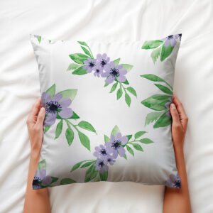 Widok z góry: dłonie trzymają poduszkę z fioletowymi kwiatami i zielonymi liśćmi