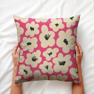Ręce trzymające poduszkę z motywem kremowych kwiatów na malinowym tle na pościeli