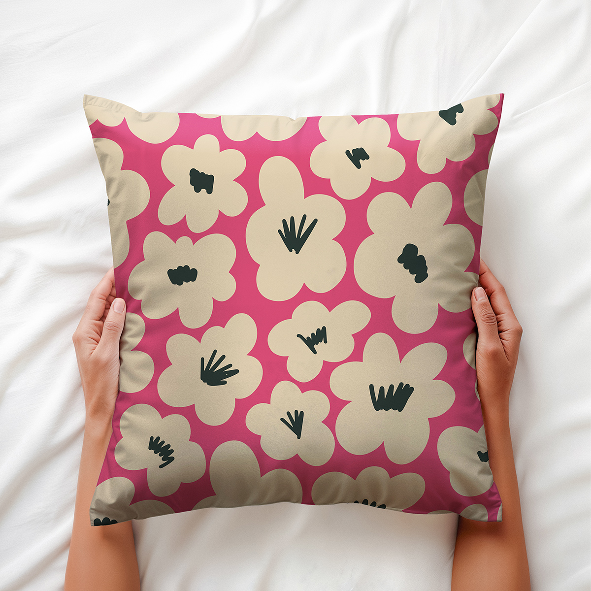 Ręce trzymające poduszkę z motywem kremowych kwiatów na malinowym tle na pościeli