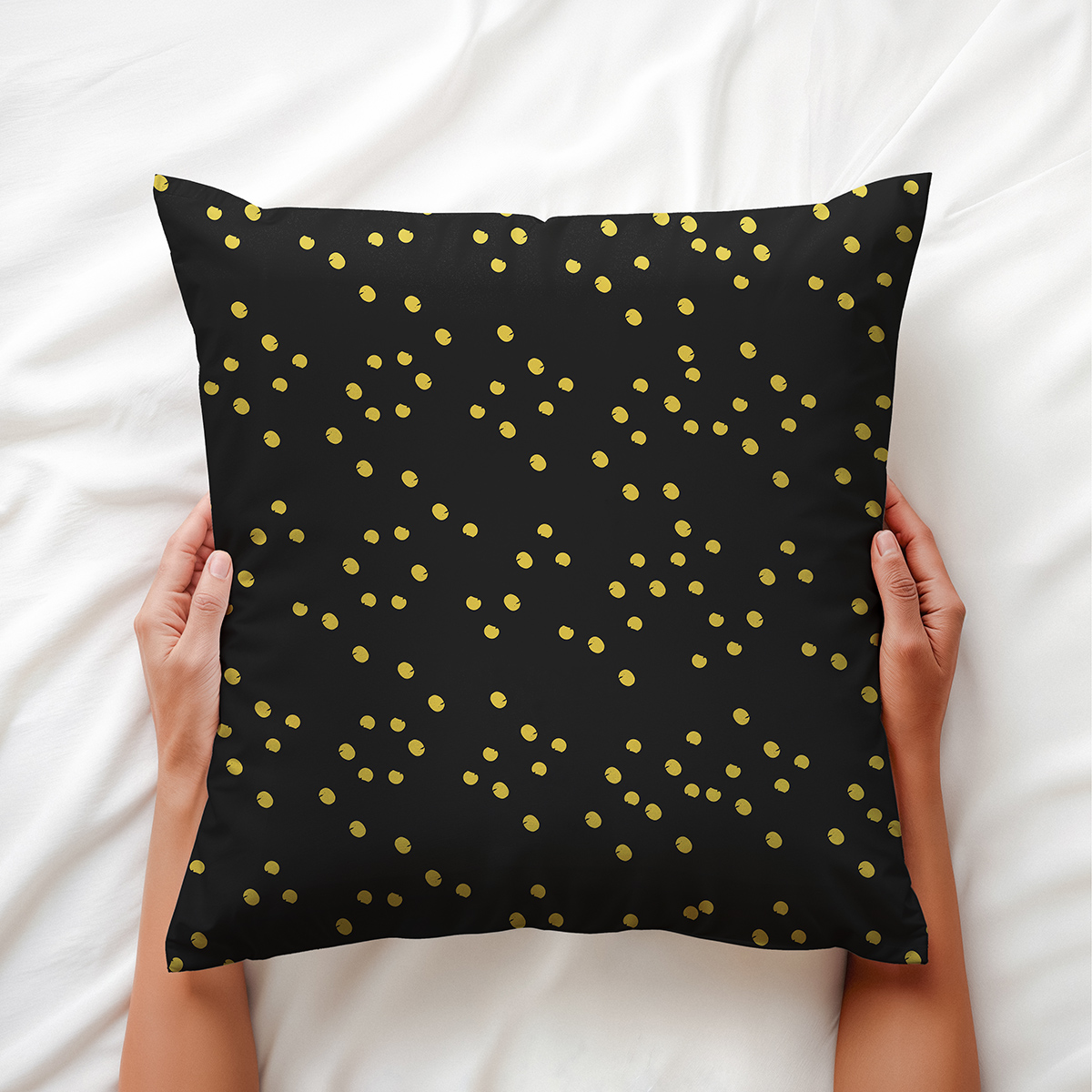 Ręce trzymające poduszkę z drobnym wzorem złotych kropek na łóżku