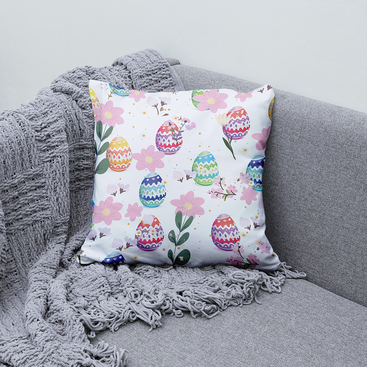 Poduszka z pastelowymi pisankami ułożona na szarym kocu na kanapie, aranżacja wnętrza
