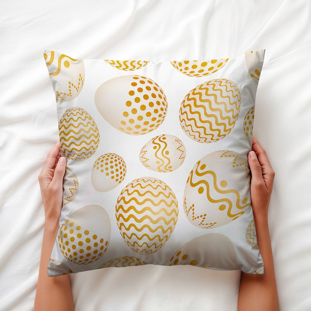 ręce trzymające poduszkę z motywem złotych pisanek na jasnej pościeli