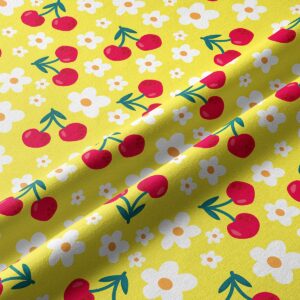 Zbliżenie tkaniny pokazujące detal czerwonych wiśni i białych stokrotek na żółtym tle