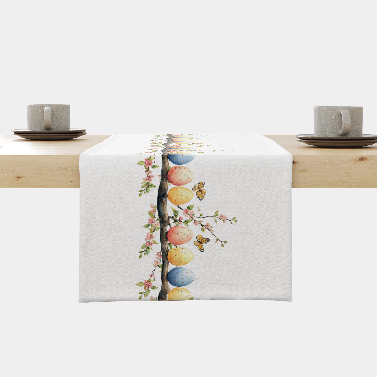 Bieżnik rozłożony na stole z rzędem pastelowych pisanek na gałązce i kwitnącymi różowymi kwiatami