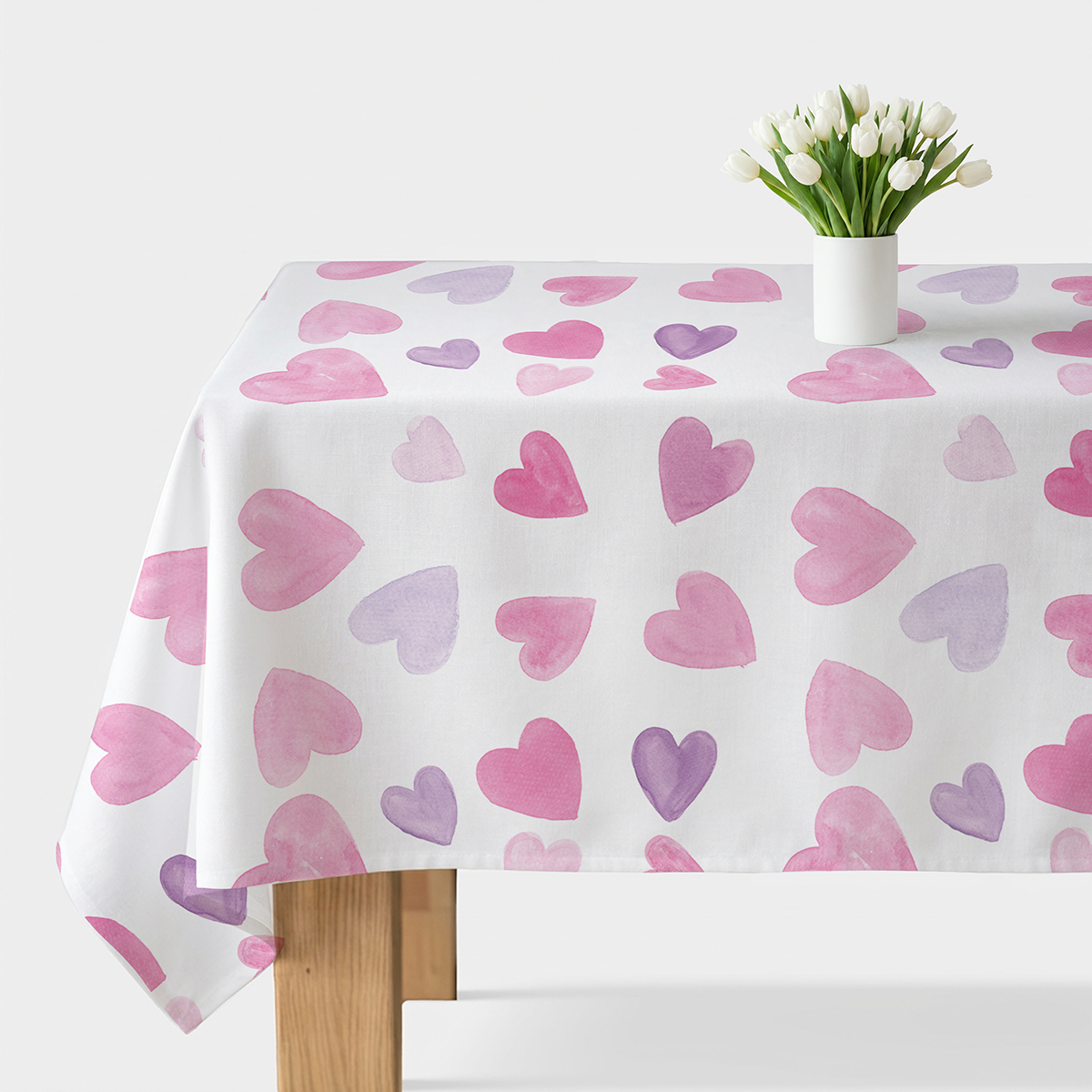 obrus z białym tłem i różowo-fioletowymi akwarelowymi sercami na stole z wazonem białych tulipanów