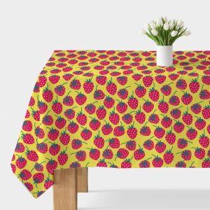 Obrus z żywym wzorem truskawek na żółtym tle rozłożony na stole, widok ogólny