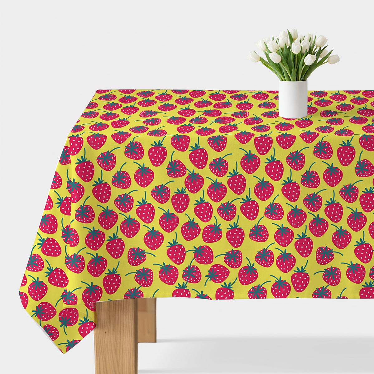 Obrus z żywym wzorem truskawek na żółtym tle rozłożony na stole, widok ogólny