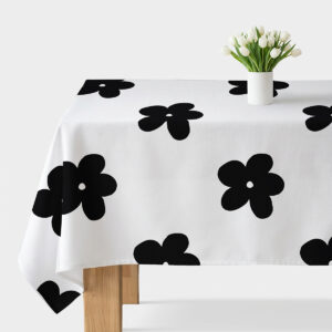 biały obrus z dużymi czarnymi kwiatami rozłożony na stole z białym wazonem z tulipanami
