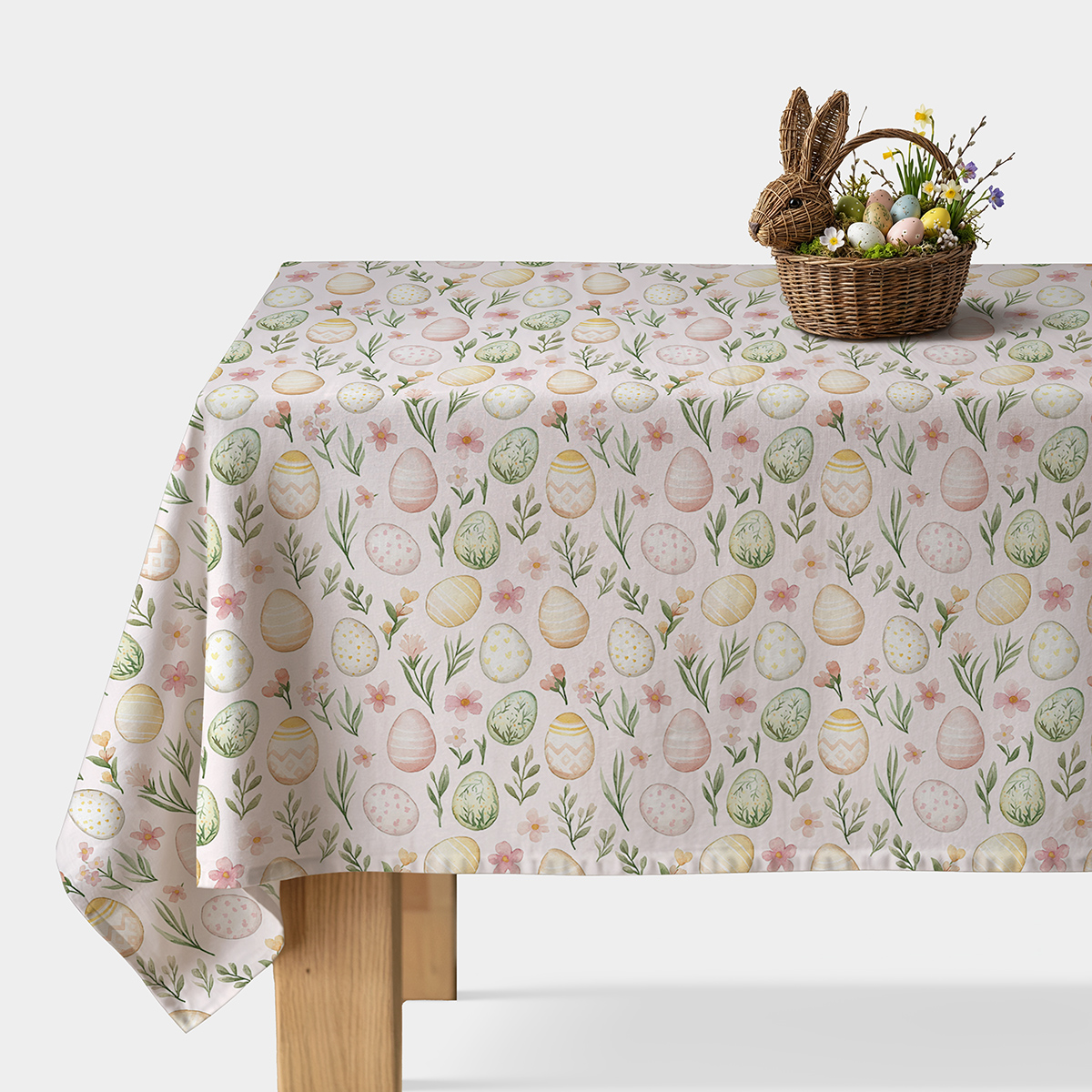 obrus z pastelowymi pisankami na stole z wiklinowym koszykiem i dekoracyjnym króliczkiem