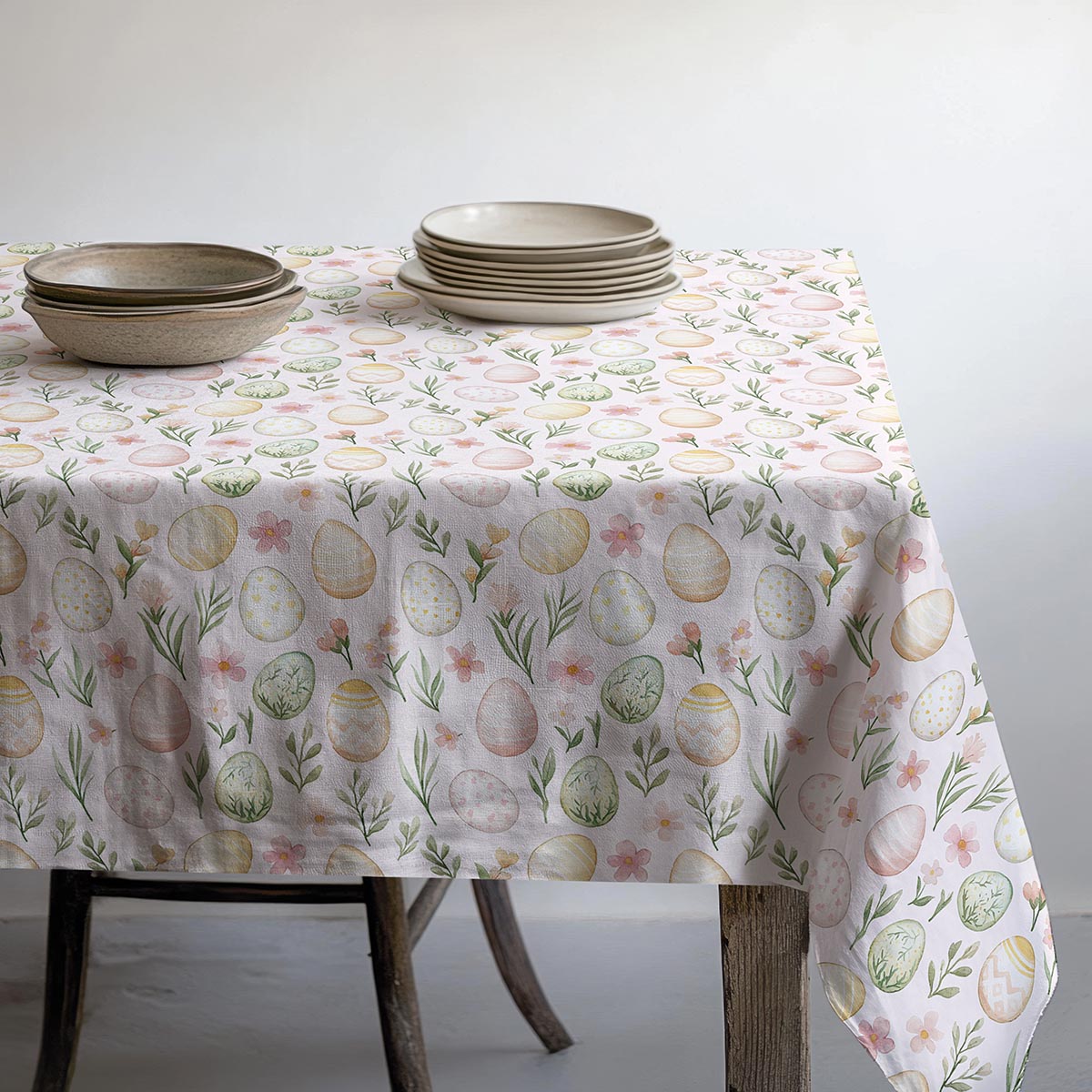 stół nakryty obrusm z motywem pisanek z ułożonymi talerzami i misami