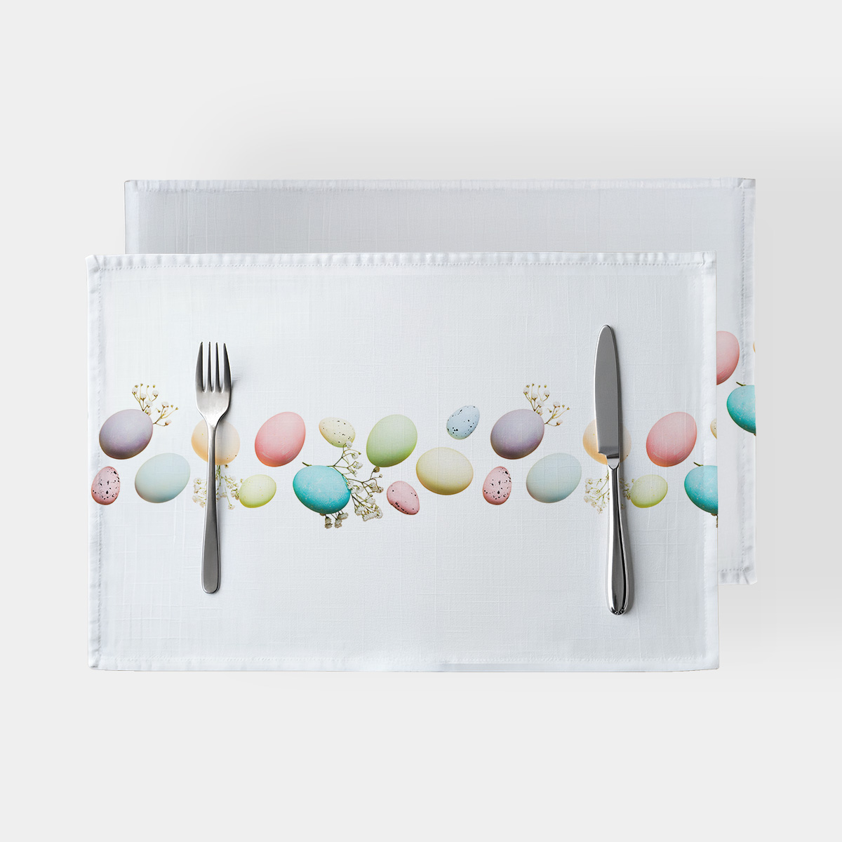 biała podkładka z poziomym pasem pastelowych pisanek i sztućcami ułożonymi na stole