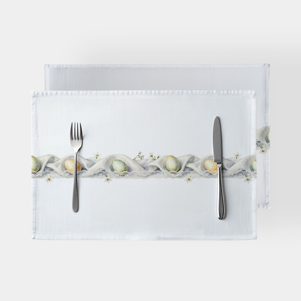 Podkładki z koronkową girlandą i pastelowymi pisankami na białym tle z widocznymi sztućcami