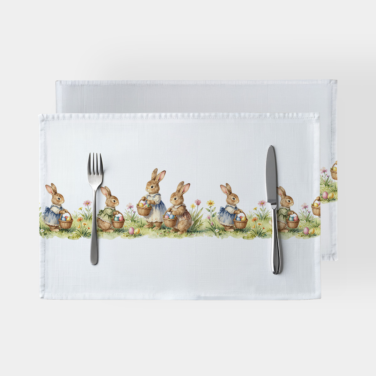 Widok z góry na białe podkładki z nadrukiem zajączków niosących koszyki z pisankami, ułożone z sztućcami