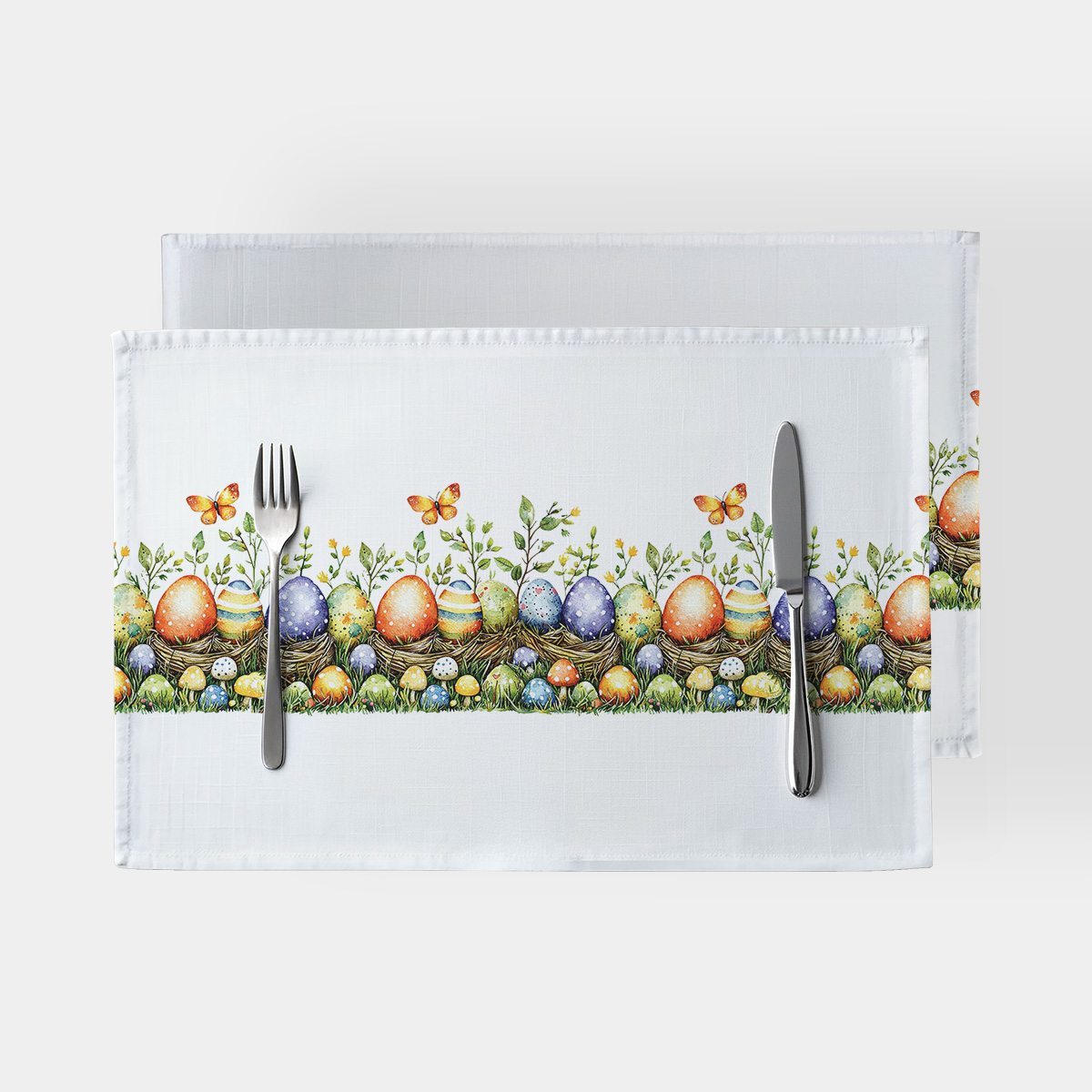 biała podkładka z pasem kolorowych pisanek, gniazdek i motylków widok z góry z sztućcami