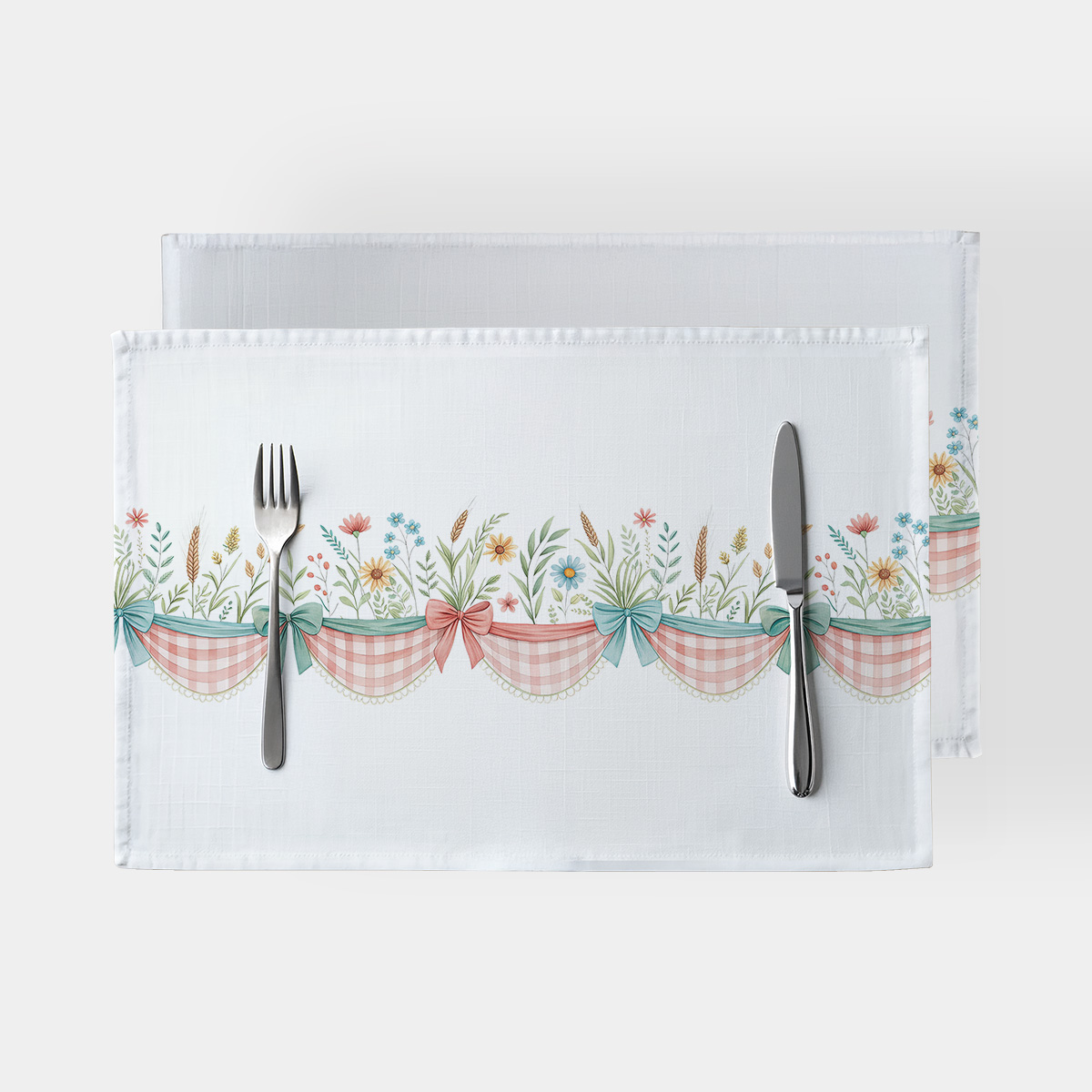 Białe podkładki z dekoracyjnym pasmem w kratkę, kokardami i polnymi kwiatami, widok z góry z sztućcami