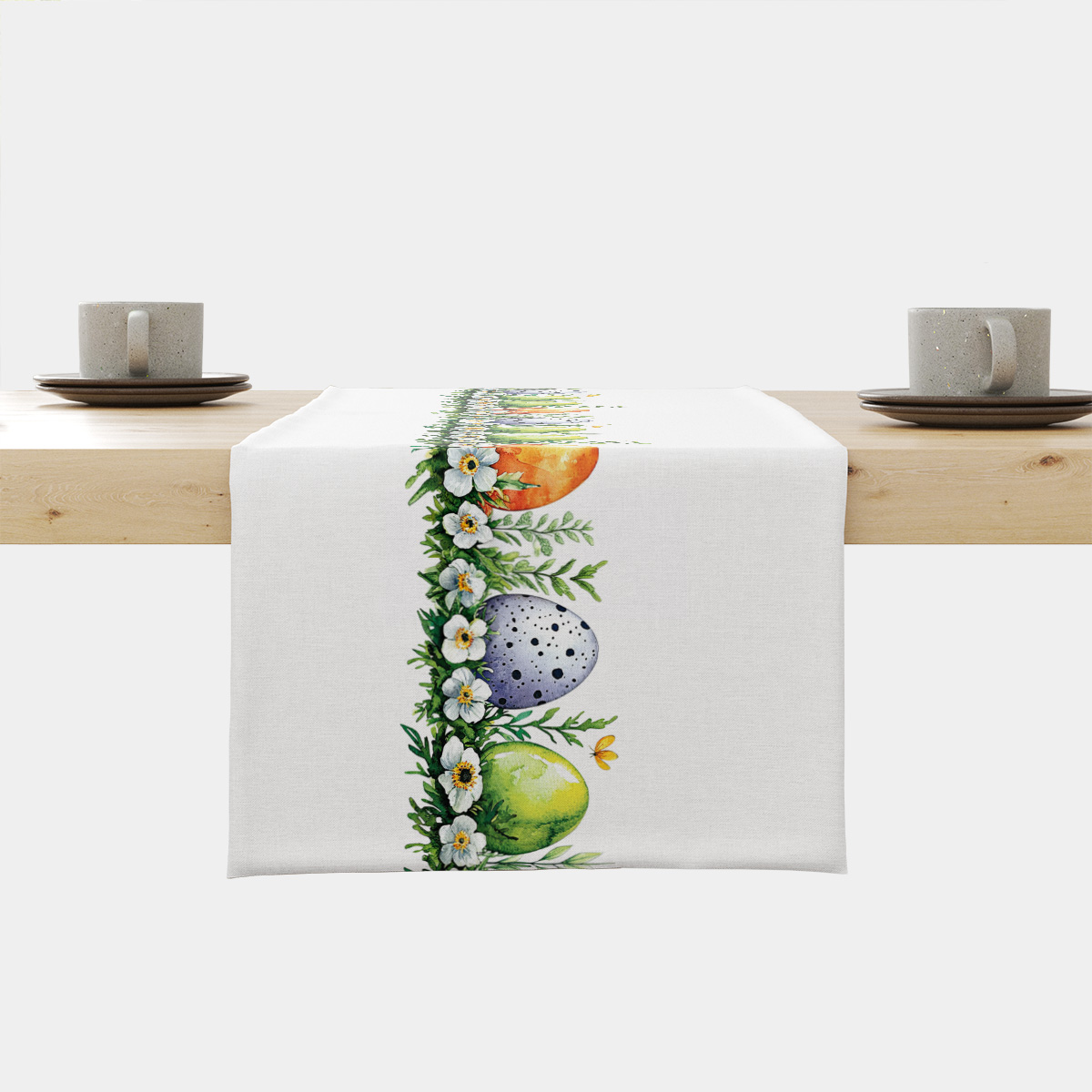 biały bieżnik z centralną girlandą pisanek i białych kwiatów rozłożony na drewnianym stole