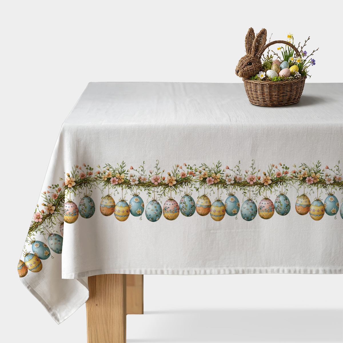 biały obrus z dekoracyjnym pasem malowanych pisanek i kwiatowej girlandy rozłożony na stole, widok z przodu