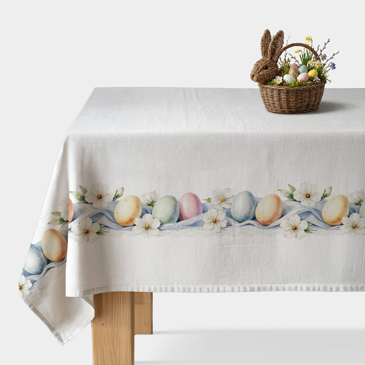 obrus rozłożony na stole z pasem pastelowych pisanek i białych kwiatów, widok z przodu