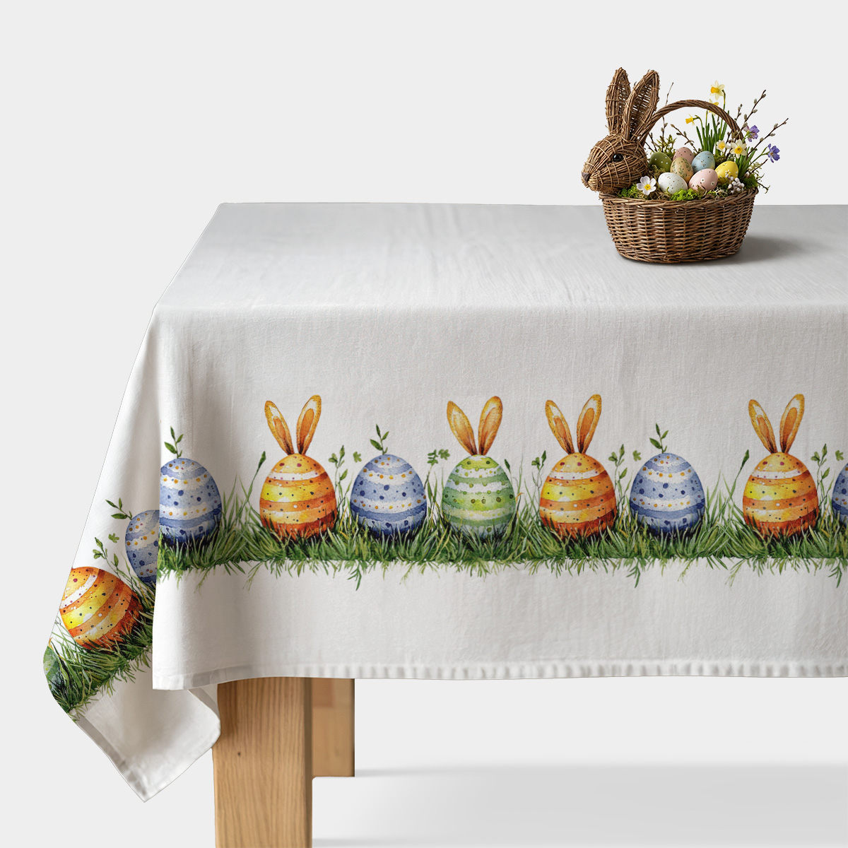 Obraz główny: biały obrus z rysunkowym paskiem kolorowych jajek z króliczymi uszami i trawą biegnącym wzdłuż krawędzi stołu