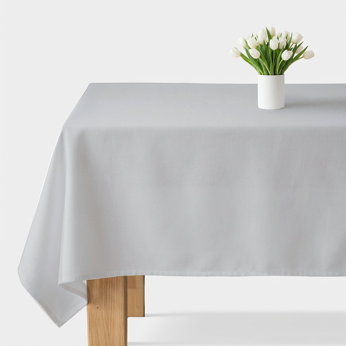 Jasnoszary obrus rozłożony na stole z białym wazonem tulipanów