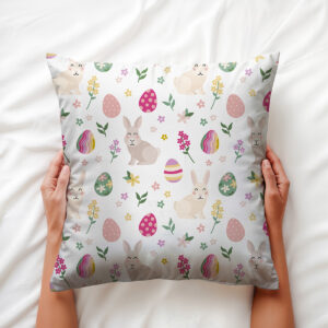 Ręce trzymające poduszkę z motywem zajączków i kolorowych pisanek, widok z góry
