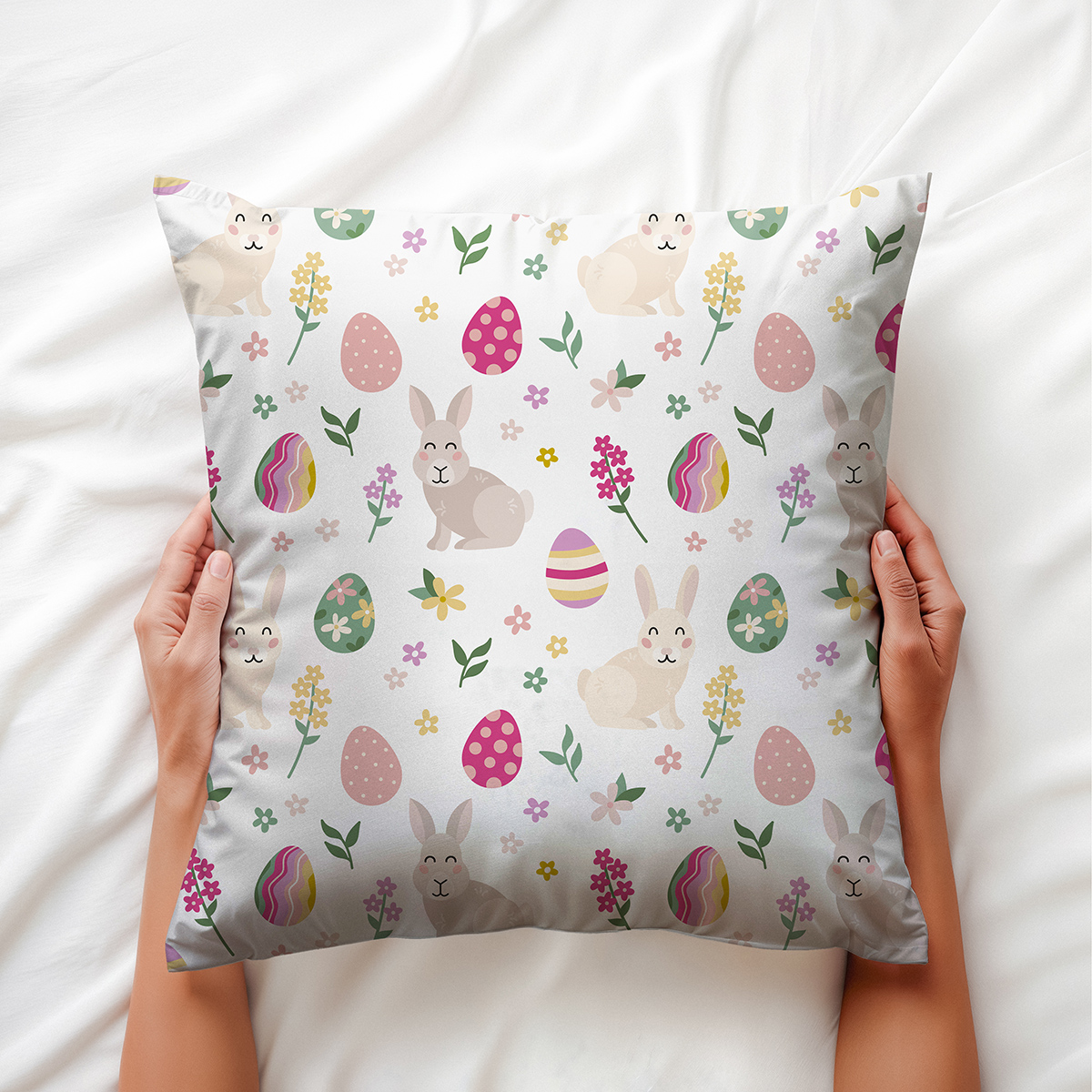 Ręce trzymające poduszkę z motywem zajączków i kolorowych pisanek, widok z góry