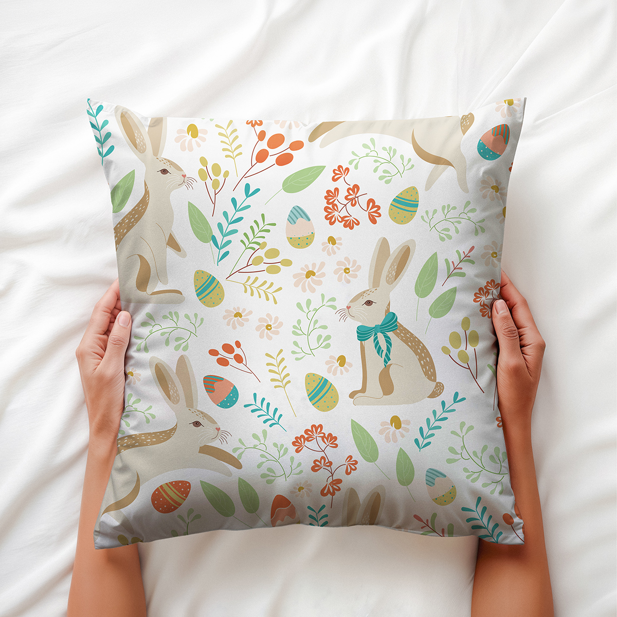 Dłonie trzymające poduszkę z motywem zajączków i kwiatów na pościeli — ujęcie aranżacyjne